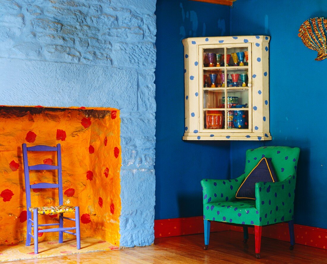 Polstersessel in bunt bemalten eklektischen Zimmer mit blauen Wänden und orangefarbener Kaminnische
