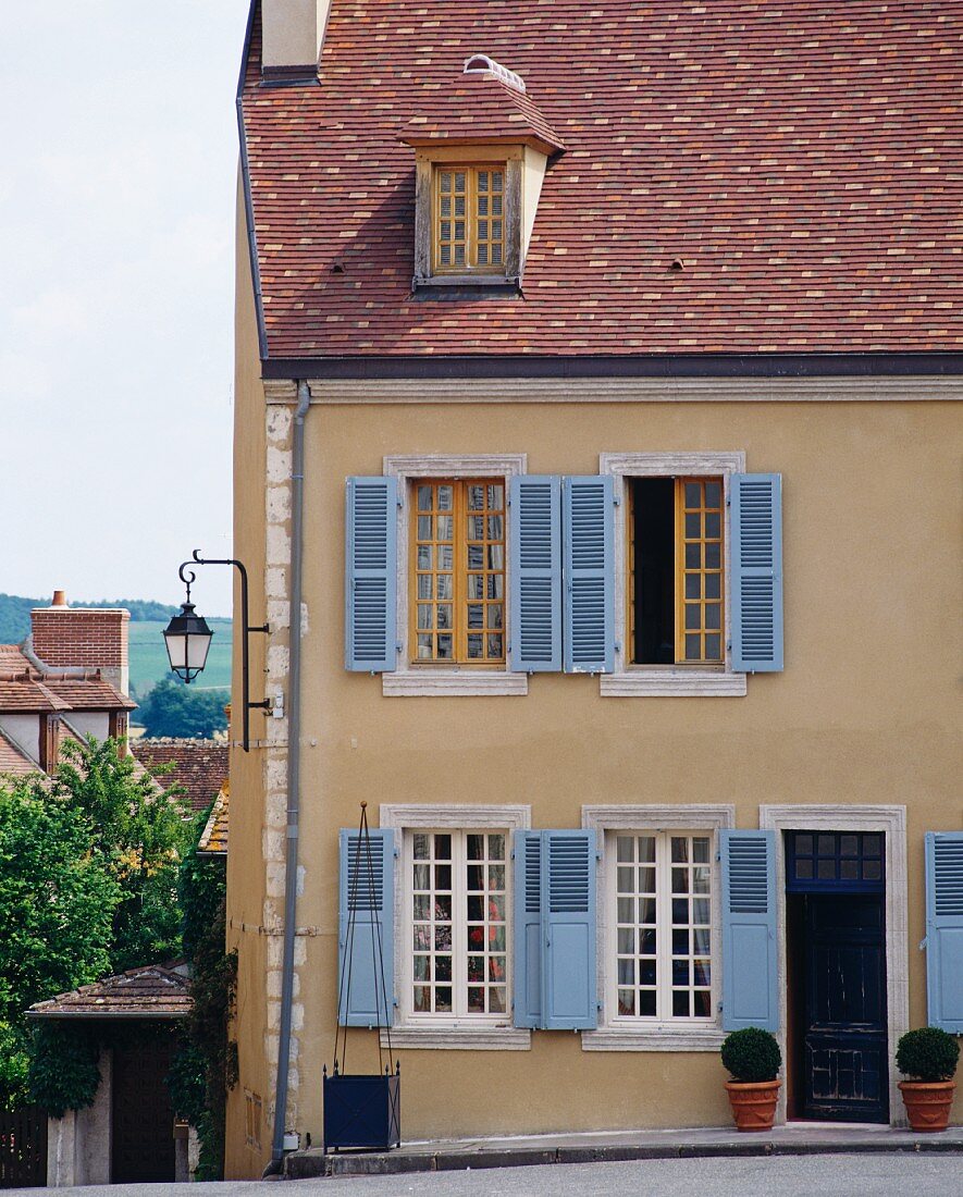 Fassade eines beigen Wohnhauses mit blauen Fensterläden (Frankreich)