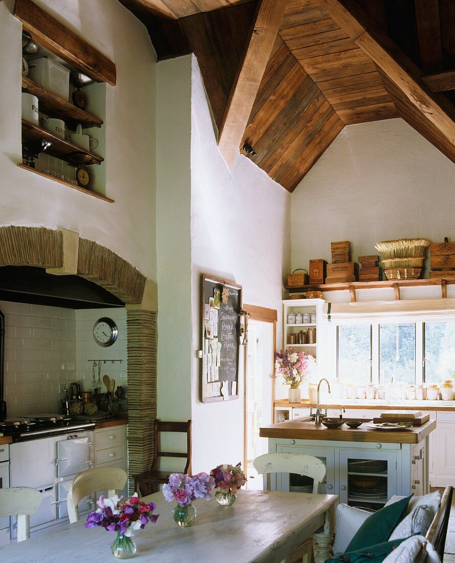 Landhausküche mit gewölbter Holzdecke, Esstisch mit Stühlen & Herd in gefliester Nische