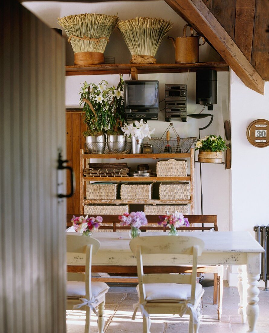 Blick durch geöffnete Tür in Landhausküche mit Esstisch, Stühlen, Holzbank & Utensilien in Wandregalen