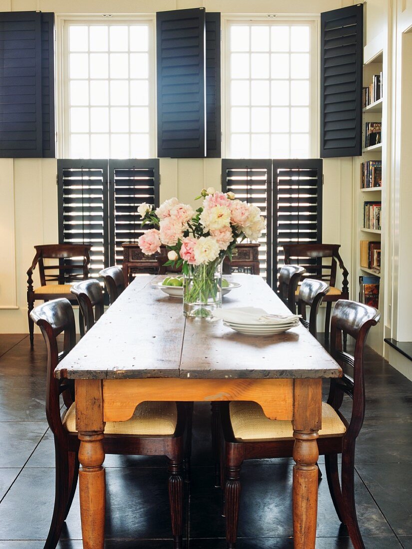 Rustikaler Tisch mit Stühlen aus dunklem, geschwungenem Holz vor dem Fenster mit blauen Innenläden
