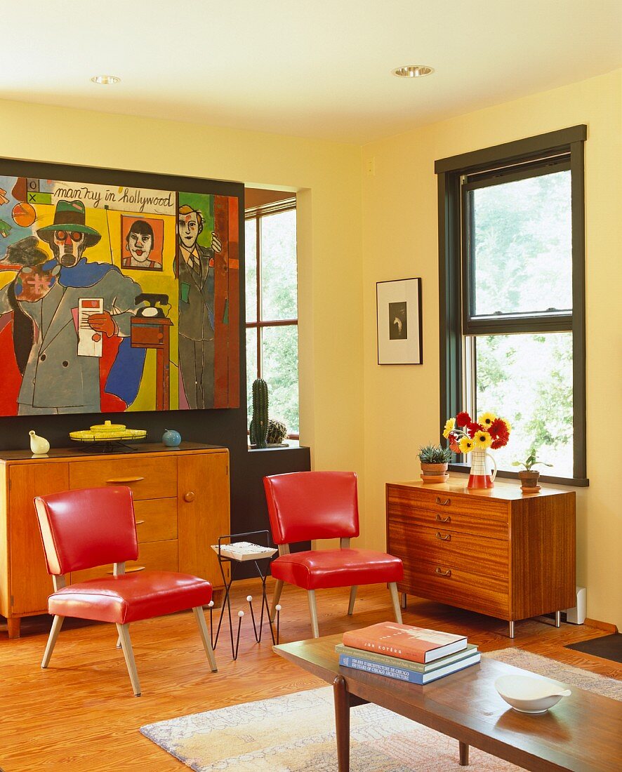 Gelbgetöntes Wohnzimmer mit roten Polsterstühlen im 50er Jahre Stil und bunte Malerei