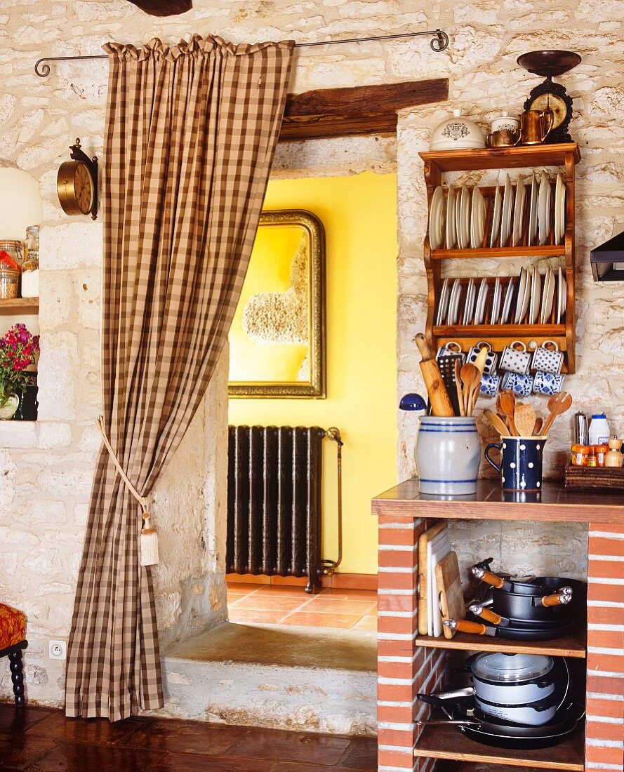 Rustikale Küche in mediterranem Haus - Blick durch offenen Durchgang mit gerafftem Vorhang in den Flur