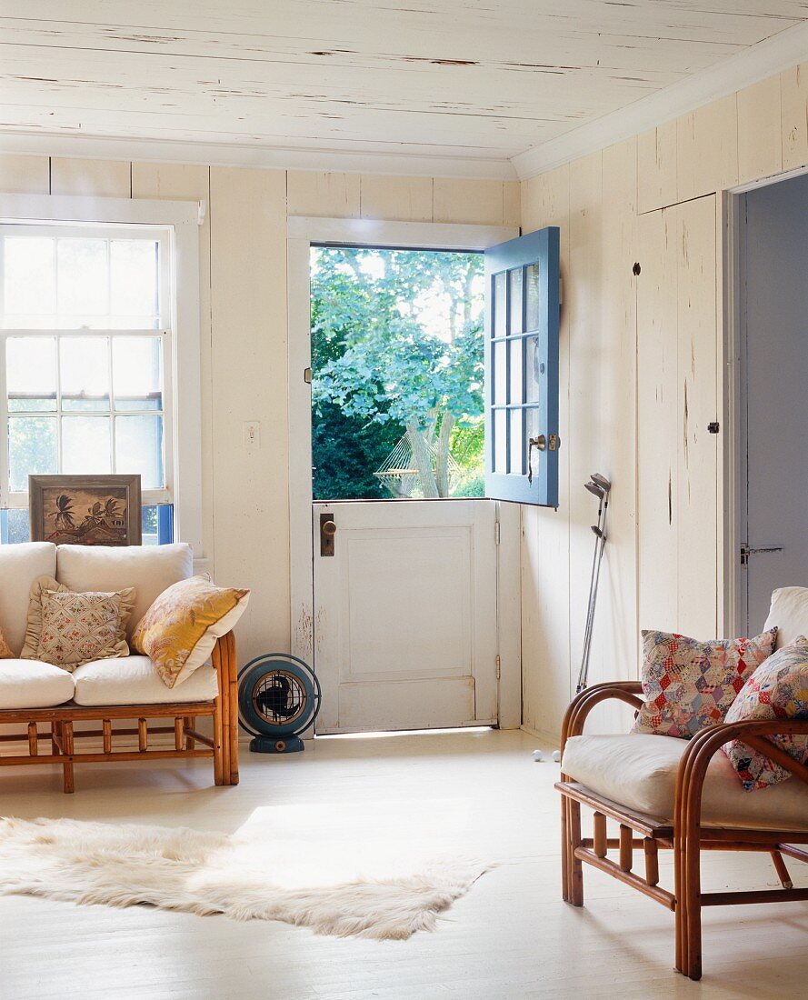 Leichte Rattanmöbel mit Polstern im Wohnzimmer eines Landhauses und zweigeteilte Tür mit offenem Flügel