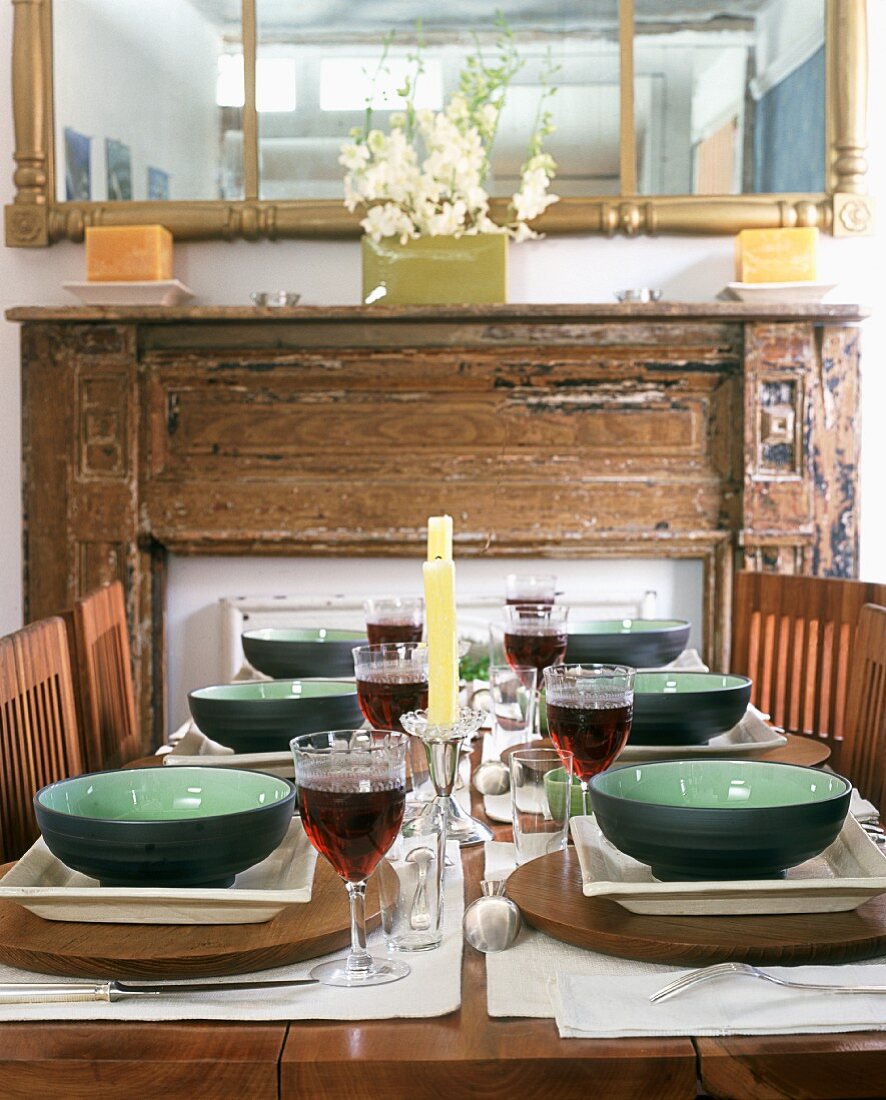Gedecke und gefüllte Rotweingläser auf dem Tisch vor Kamin mit rustikaler Holz-Kaminschürze
