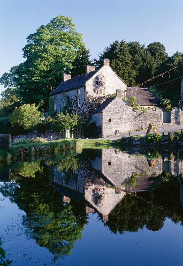 Kleiner See mit perfekter Spiegelung des dahinterliegenden englischen Landhauses mit Natursteinfassade