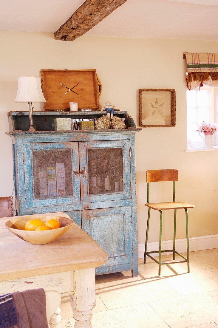 Vitrinenschrank im Vintagelook mit blauer Patina und Retro Kinderhochstuhl in einfacher Landhausküche