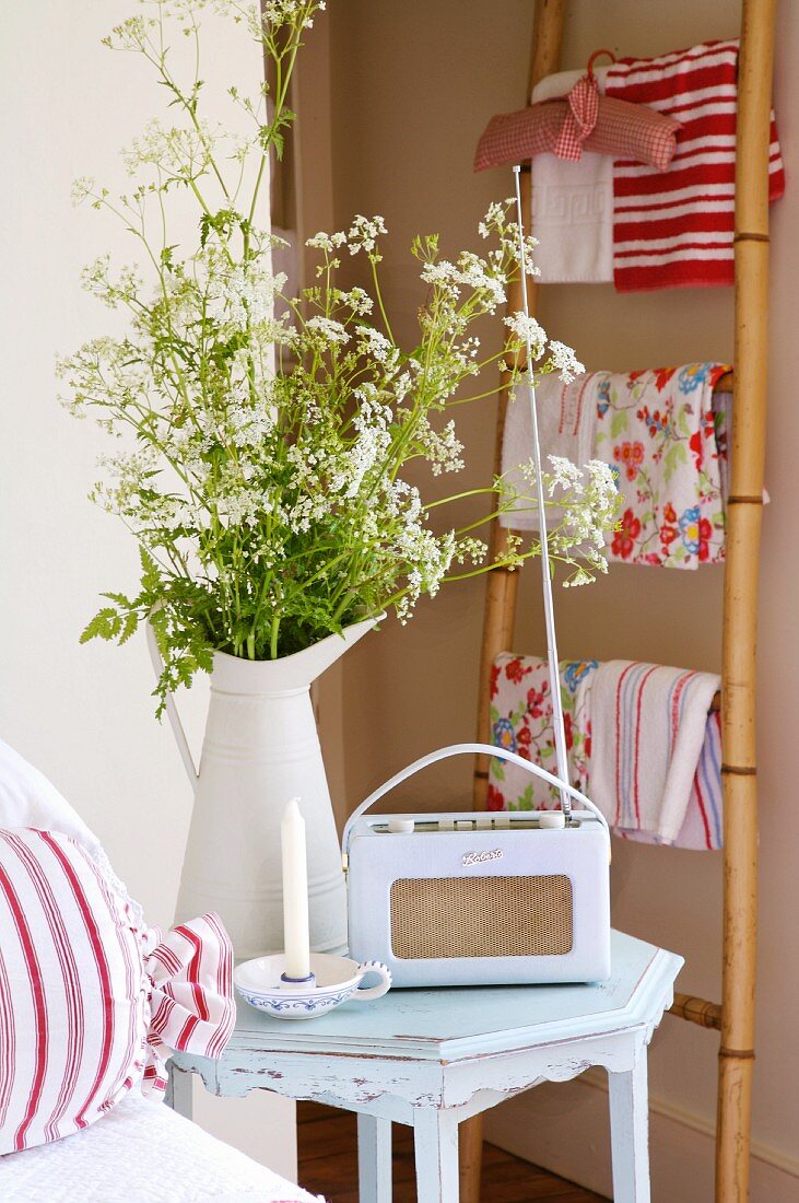 Kofferradio im Retrostil und Wiesenblumenstrauss auf Nachttisch; Handtücher an Bambusleiter im Hintergrund