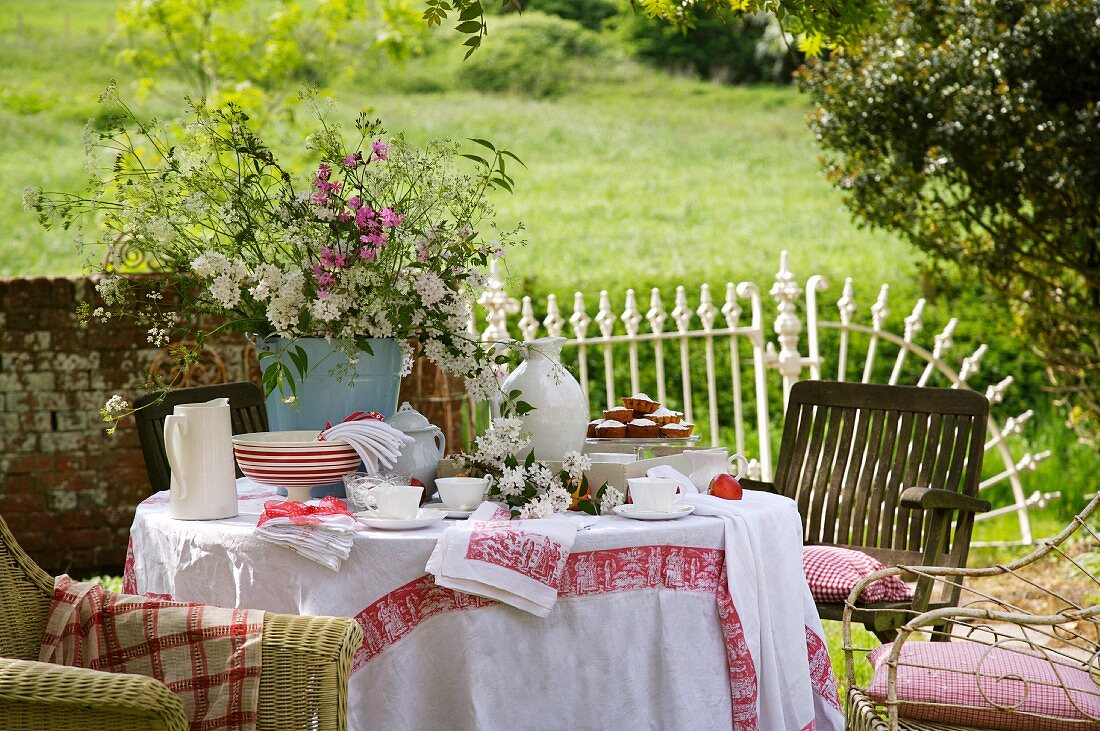 Gedeckter Tisch für den Nachmittagstee im Garten mit Wiesenblumenstrauss und rotweiss gemusterten Stoffen