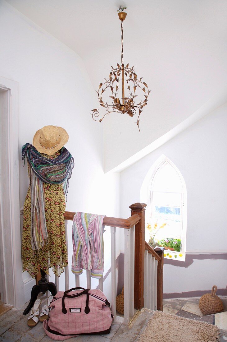 Kleid, Schal und Strohhut an Garderobenständer auf dem oberstem Absatz einer Landhaustreppe; filigraner Kronleuchter mit stilisiertem Blattwerk