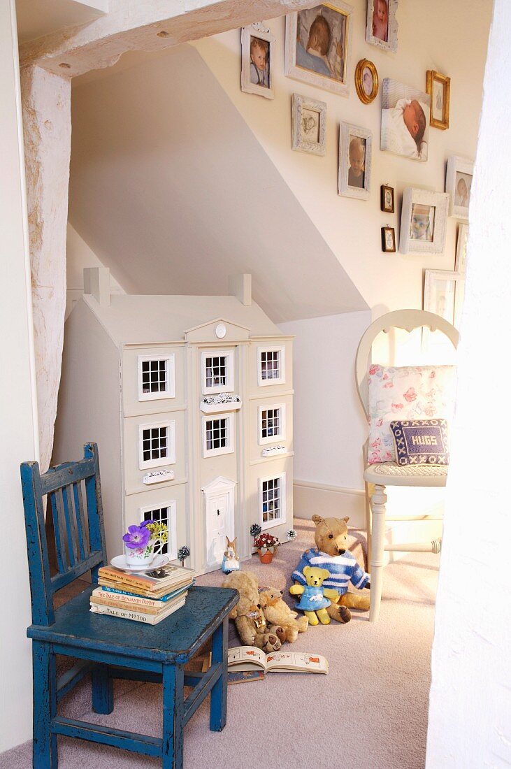 Puppenhaus im englischen Landhausstil, Plüschbären und alter, blauer Kinderstuhl mit Bücherstapel