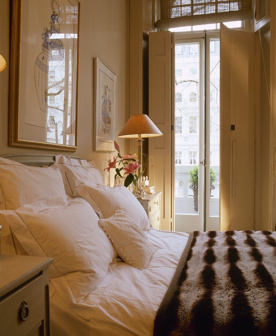 Doppelbett mit gestreifter Felldecke in cremefarbenem Schlafzimmer mit innenliegenden Klappläden vor den Balkontüren