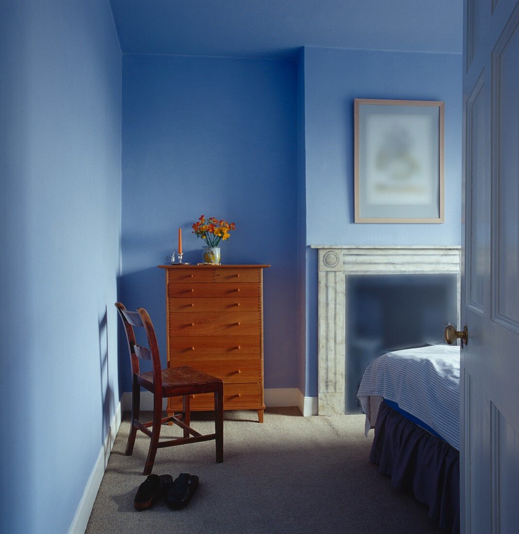 Blau getöntes Schlafzimmer mit Holzkommode neben offenem Kamin