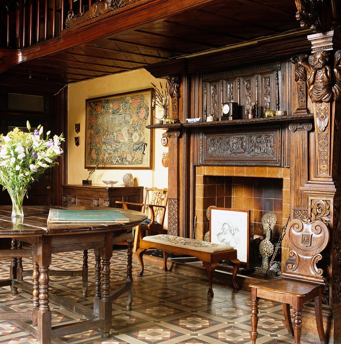Herrschaftliches Foyer mit antikem Tisch und Stühlen vor offenem Kamin mit geschnitztem Holzsims in einem Landschloss