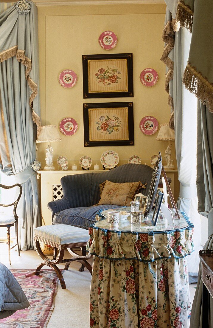 Frisiertisch mit floral gemusterter Husse vor Sessel in Schlafzimmerecke mit gehängten Wandtellern und Bilder mit Blumenmotiven