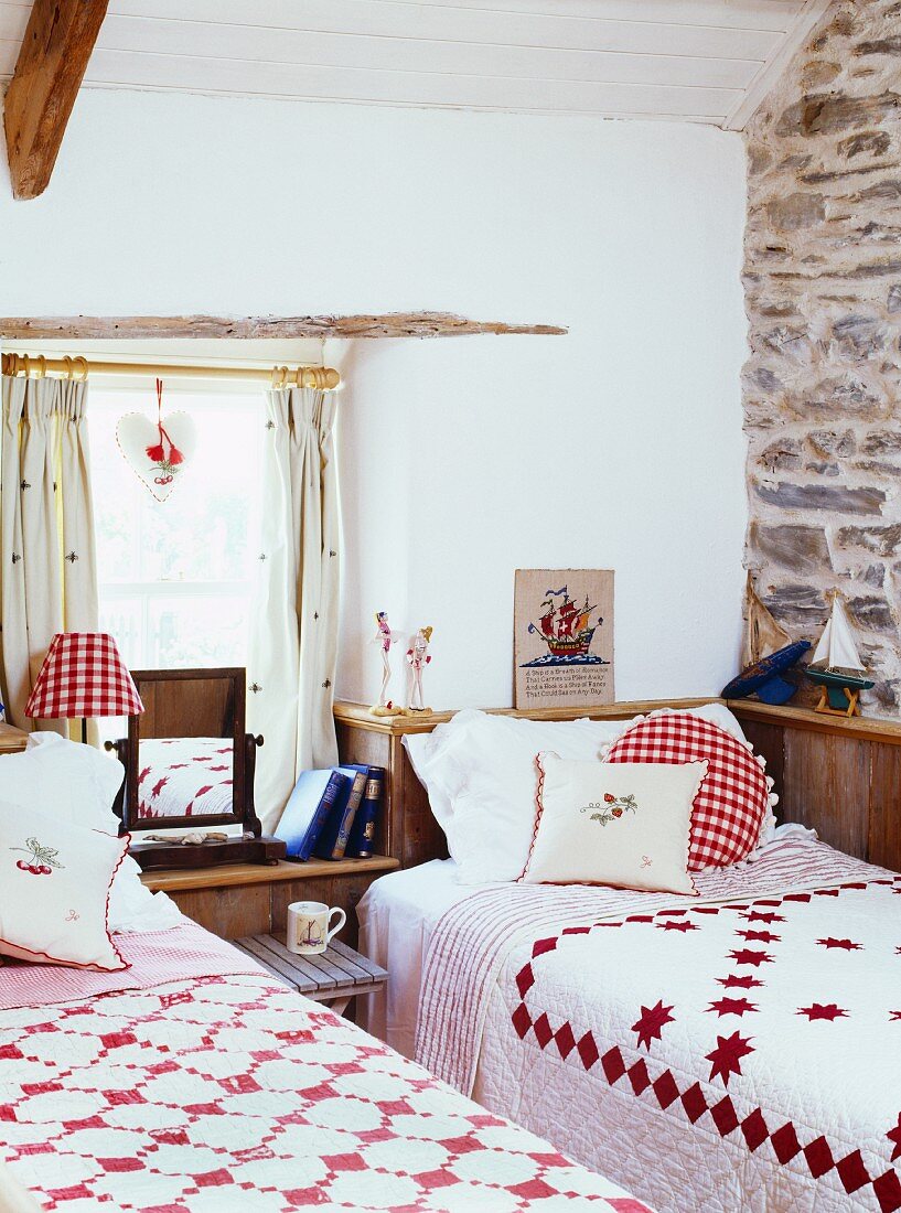 Schlafzimmer im Landhausstil mit zwei Einzelbetten mit rot-weissen Tagesdecken & Kissen