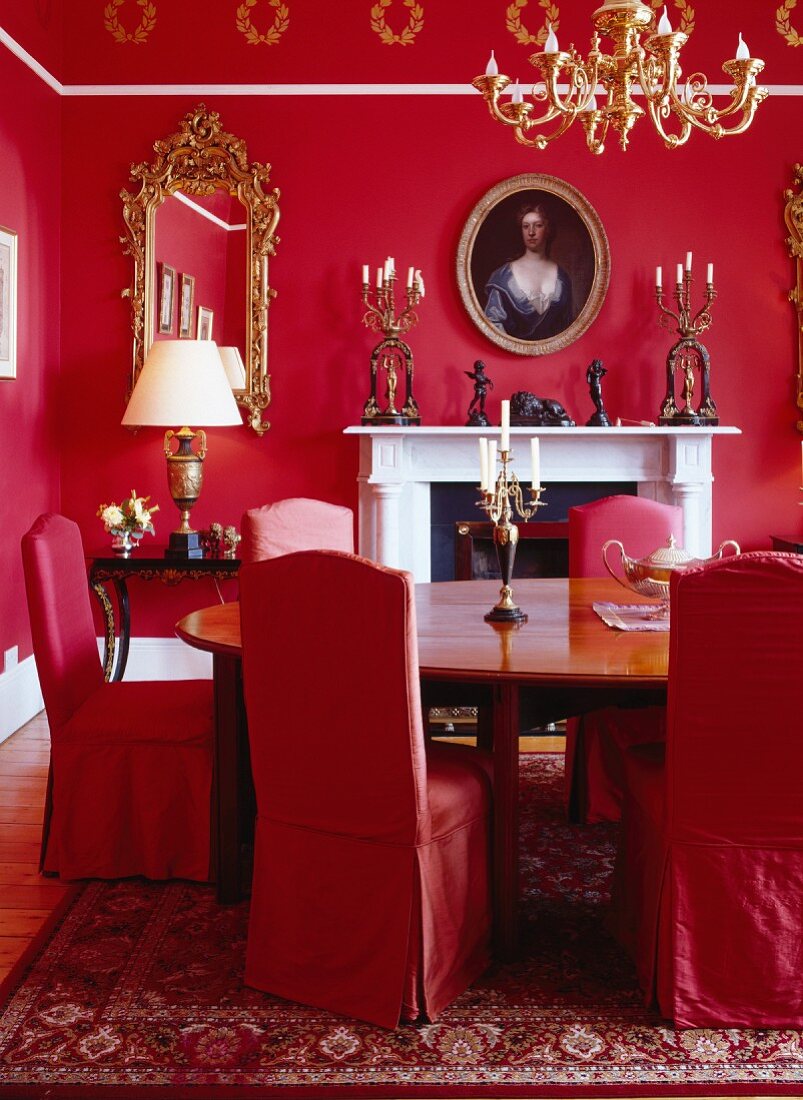 Esszimmer in Rot mit Kamin, ovalem Tisch, Stühlen mit Hussen, Kerzenleuchtern & Kronleuchter