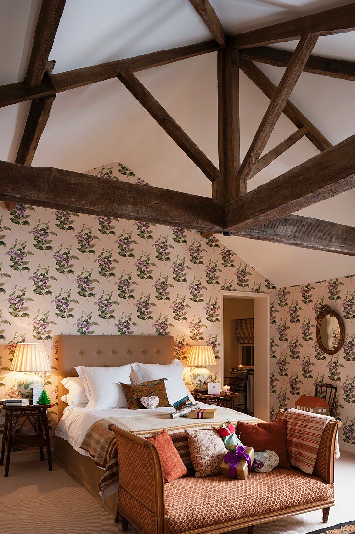 Recamiere an Bettende eines Doppelbettes an tapezierter Wand mit Blumenmotiven im rustikalen Dachgeschoss