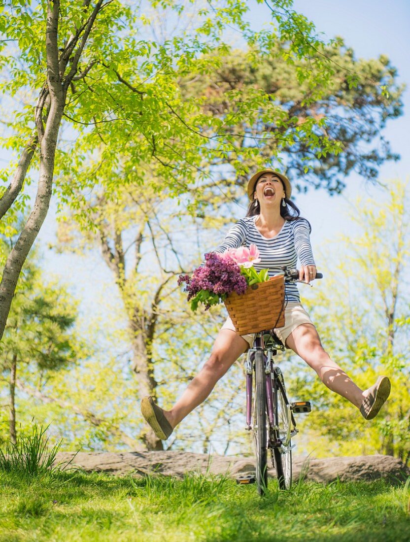 Fröhliche Frau auf Fahrrad mit Blumen im Fahrradkorb