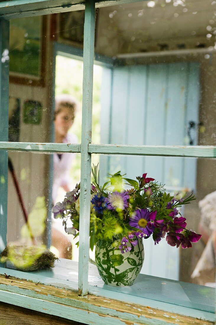 Vase of wild flowers seen through lattice window of nostalgic shepherd's hut