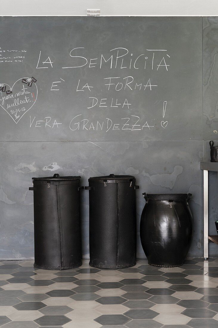 Black recycling bins made from upcycled car tyres against blackboard wall and on honeycomb tiles