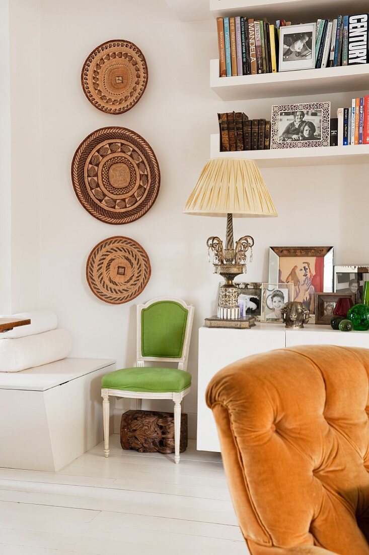 Weißes Sideboard dekoriert mit gerahmten Fotografien und eleganter antiker Tischlampe neben afrikanischer Wanddekoration