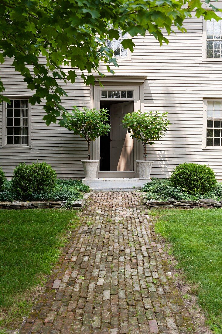 Natursteinpflasterweg zum stilvollen Eingang eines holzverkleideten, weiß gestrichenen Landhauses