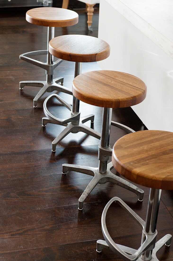 Row of vintage bar stools with round wooden seats on purist steel bases