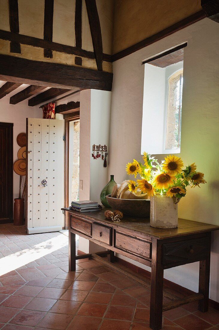 Vase of sunflowers on wooden console table in foyer of country house with terracotta floor