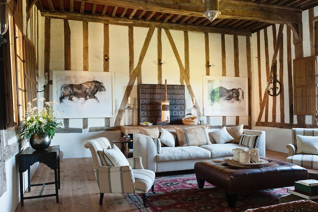 Sessel- und Sofagarnitur um Couchtisch mit braunem Lederbezug in ländlichem Wohnzimmer mit sichtbarer Fachwerkkonstruktion