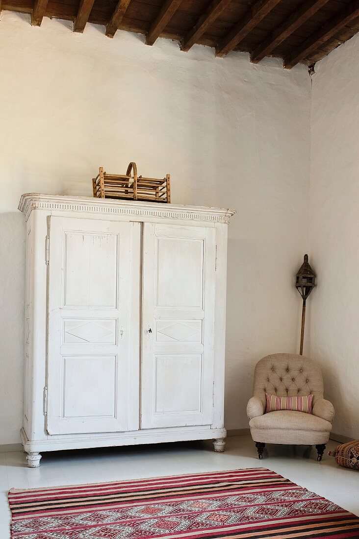 Weisser Holzschrank in geräumigen Zimmer mit hohen Decken, Sessel und marokkanischer Teppich