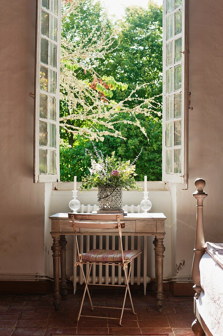 Garden chair and writing desk below open window with view of garden