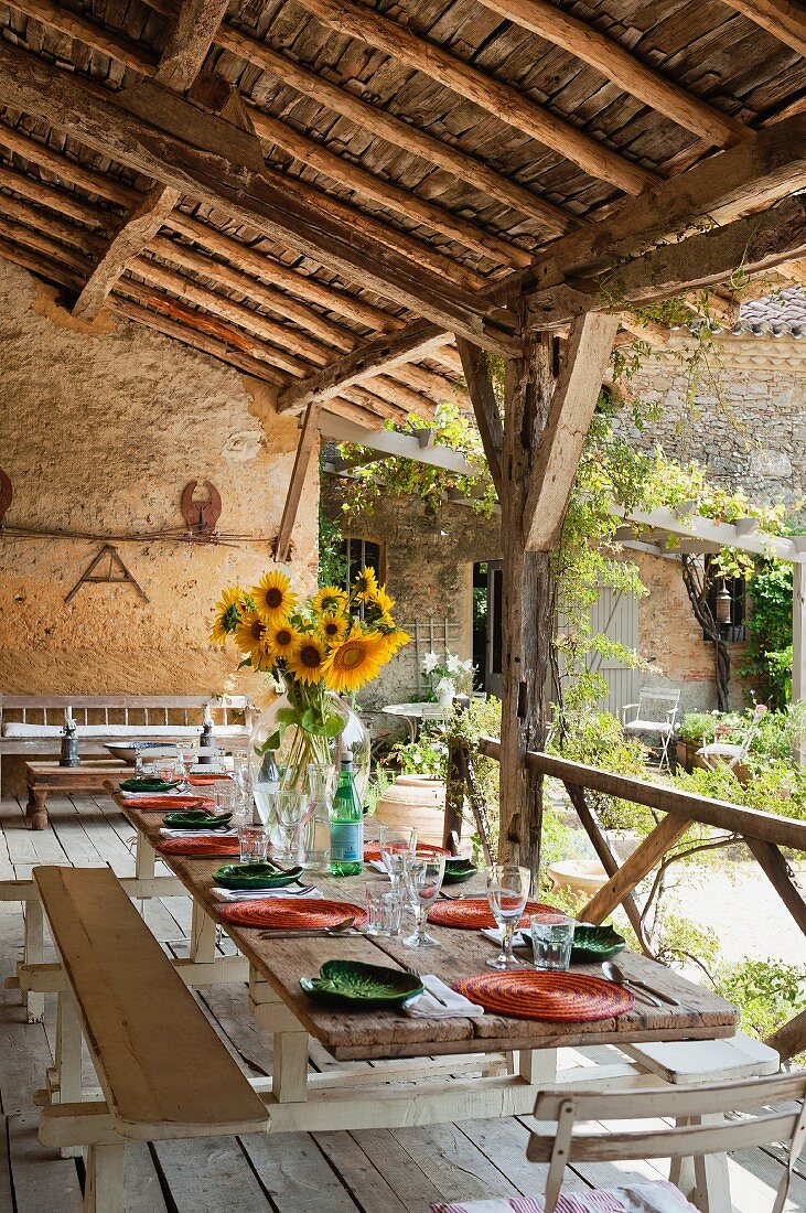 Sonnenblumenstrauss auf gedecktem Tisch mit orangen und grünen Farbakzenten auf rustikaler Veranda mit Holzdielen