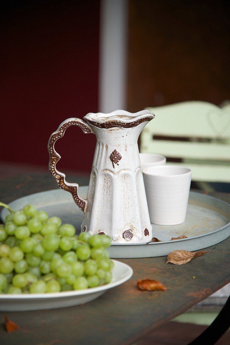 Vintage Keramikkrug und Becher auf Metalltablett, davor Teller mit Trauben