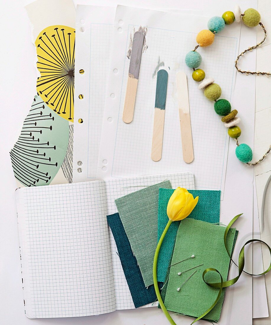 Fabric swatches in shades of green, yellow tulip, string of wooden beads and paint samples on wooden lolly sticks