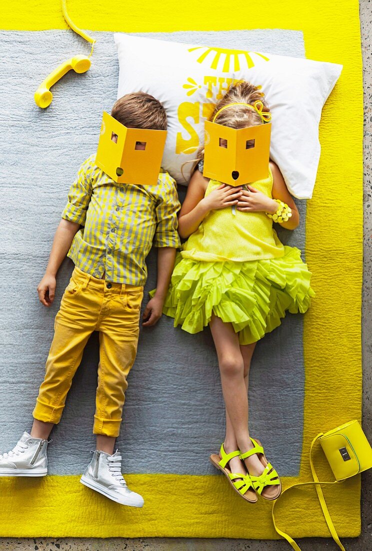 In Gelbtönen gekleidete Kinder auf einem grauen Teppich mit gelber Bordüre liegend