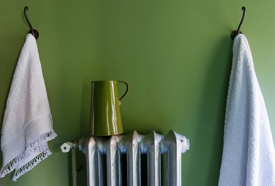 Towels on pegs & jug on radiator against green wall