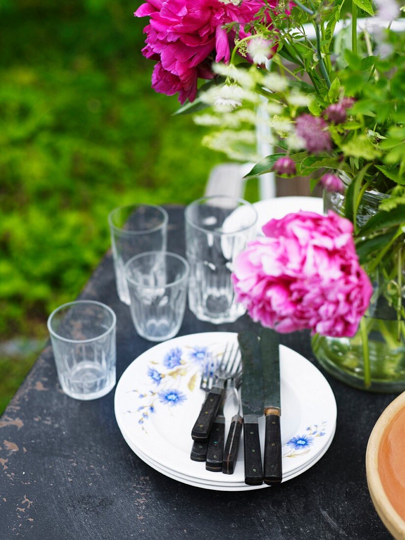 Rustikales Gedeck, Trinkgläser und Blumenstrauss auf Gartentisch
