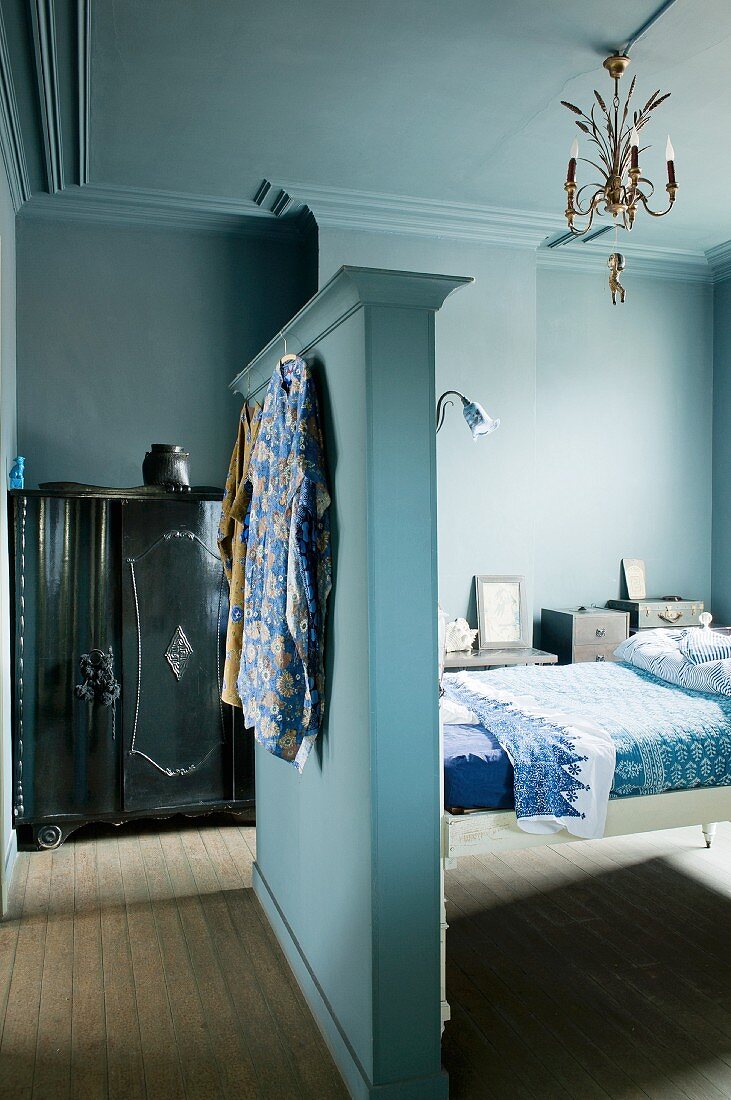 Bedroom in shades of blue with bed, partition wall as headboard & antique wardrobe