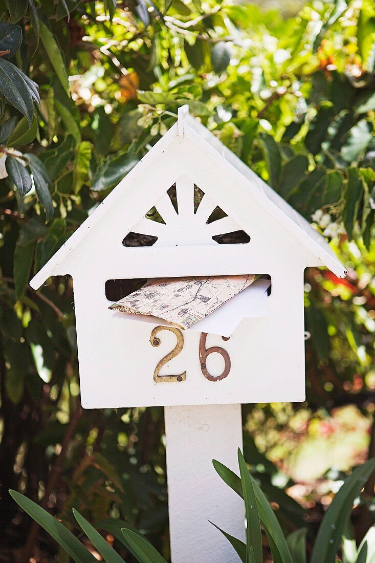 Weiß gestrichener Briefkasten in Häuschenform mit Hausnummer auf weißer Holzstütze v
