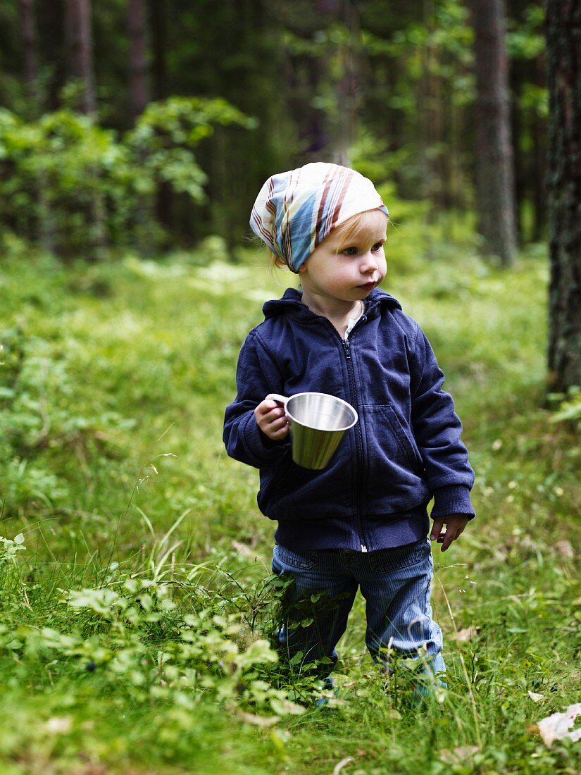 Kleines Mädchen mit Topf in der Hand im sommerlichen Wald