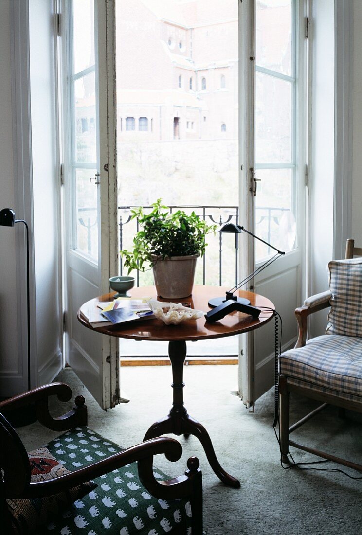 Round, vintage side table and armchairs in front of open balcony door