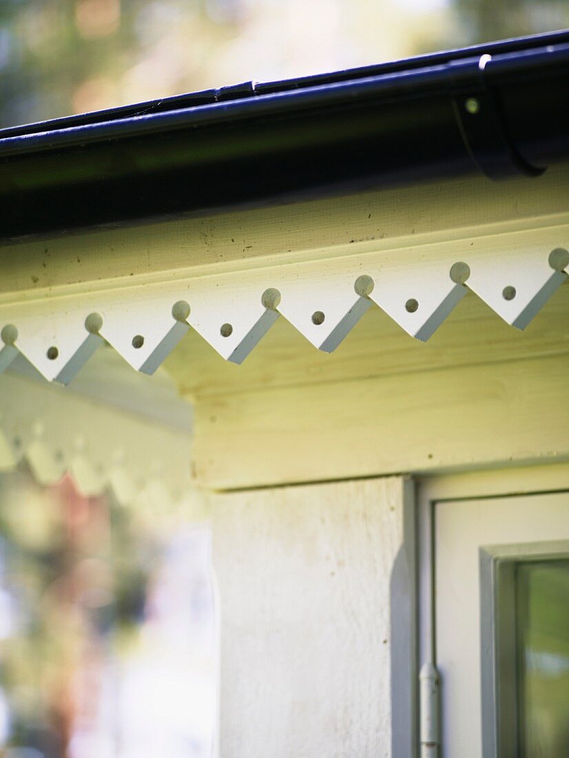Traditionelle, weiss lackierte Holzverzierung an schwedischem Vordach mit dunkler Regenrinne