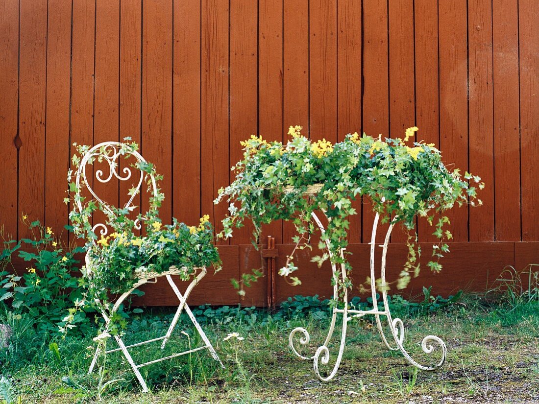 Mit Blumen und Kletterpflanzen dekorierter Gartenmöbel vor brauner Holzwand