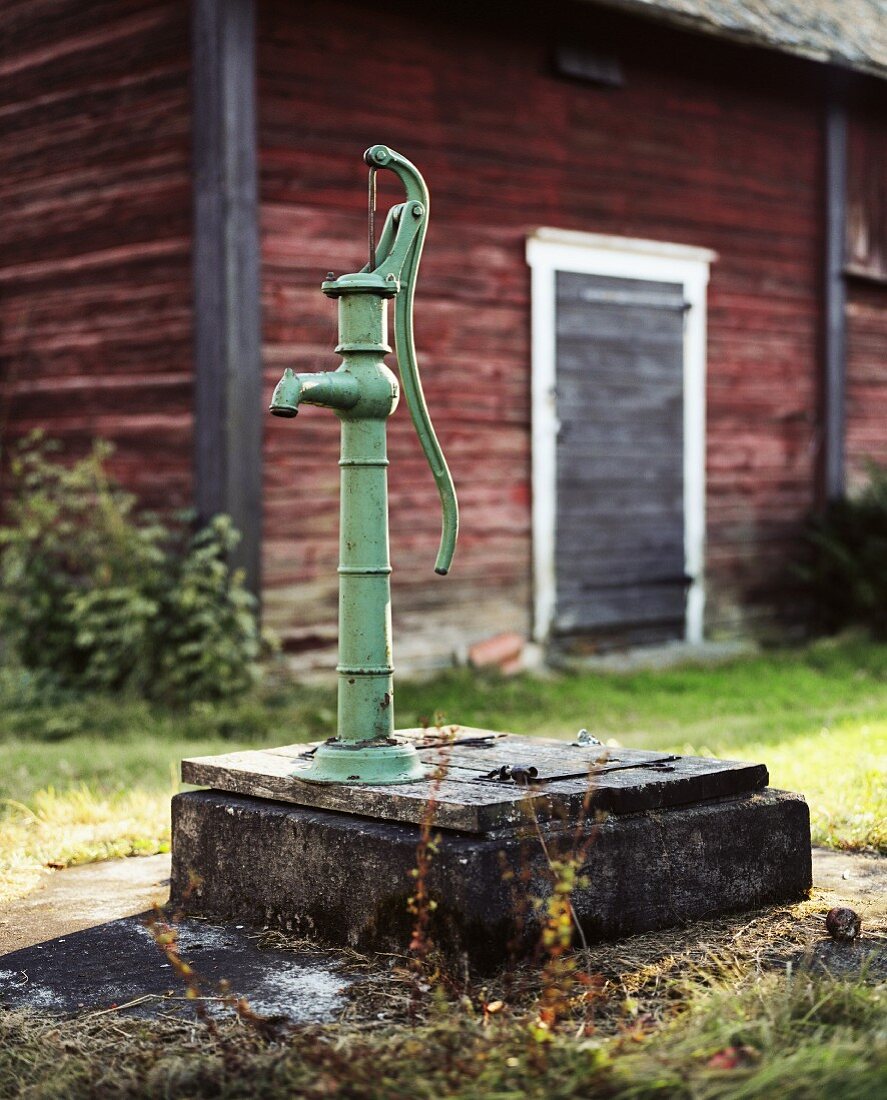 Vintage Brunnenpumpe vor Holzhütte