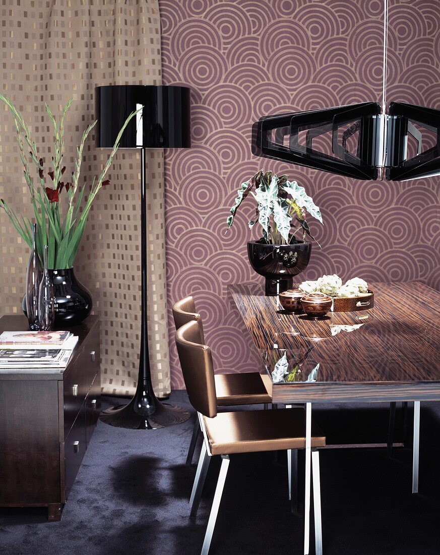 Dining table and chairs below designer pendant lamps against retro wallpaper