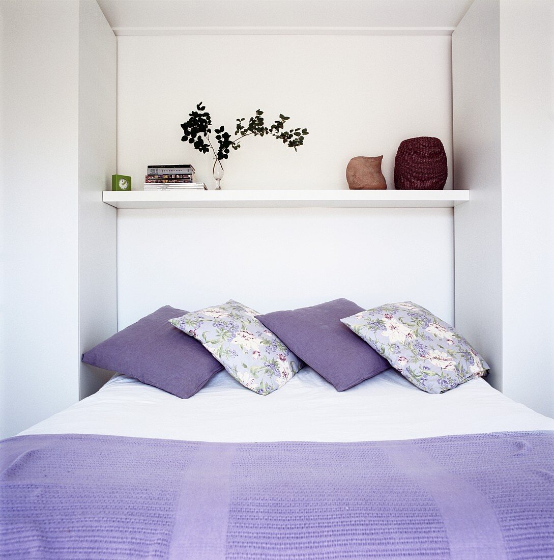 Bett mit violetter Tagesdecke und Kissen in Nische mit Regalboden