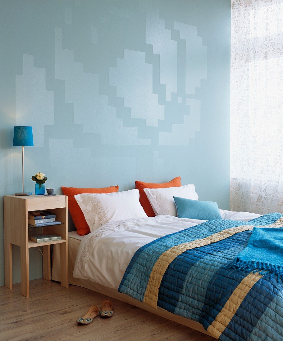Double bed with striped bedspread and modern bedside cabinet against blue wall