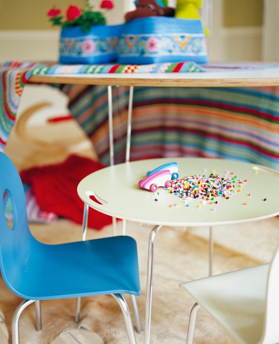Bunte Perlen und Spielzeuge auf rundem Kindertisch und blauer Stuhl