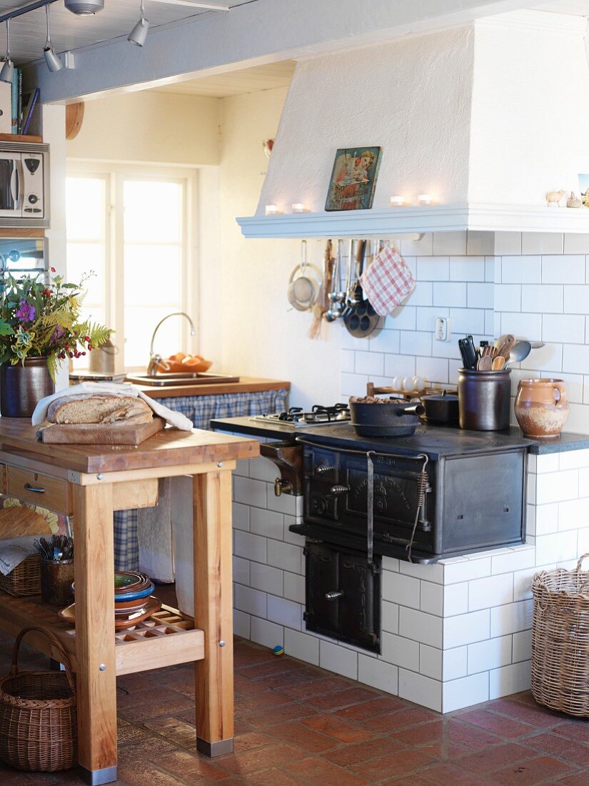 Rustic country-house kitchen with chopping block table in front of built-in, tiled oven with extractor hood